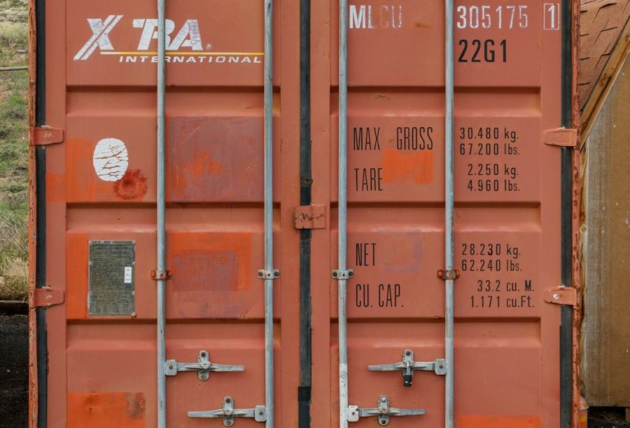 Orange 20-foot shipping container with doors closed, sitting on gravel